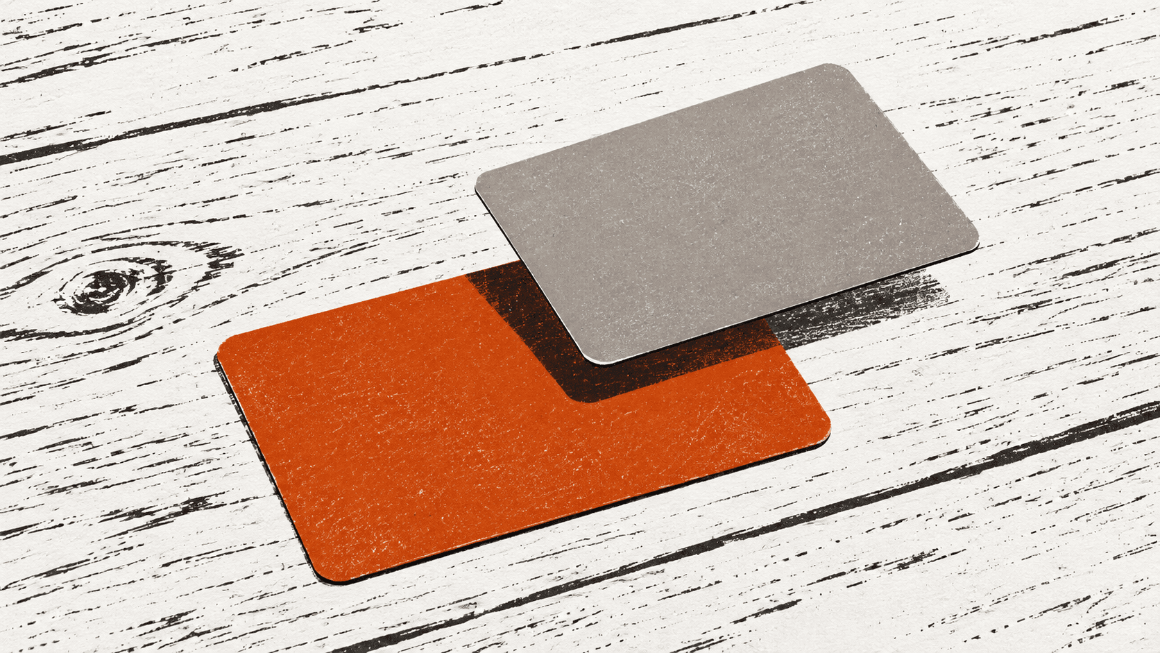 A coral bank card on a desk with a second, blank card hovering half over it, not yet fully aligned.